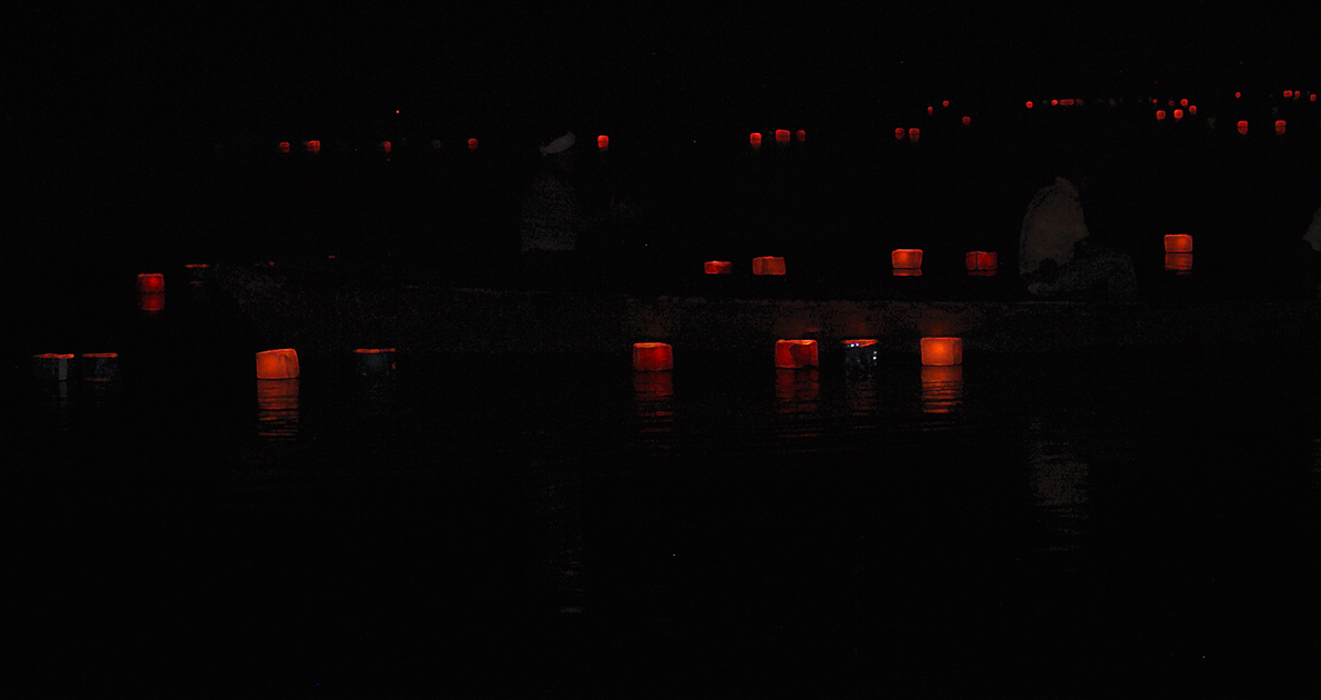 Two men in a boat putting the lanterns in the pond.