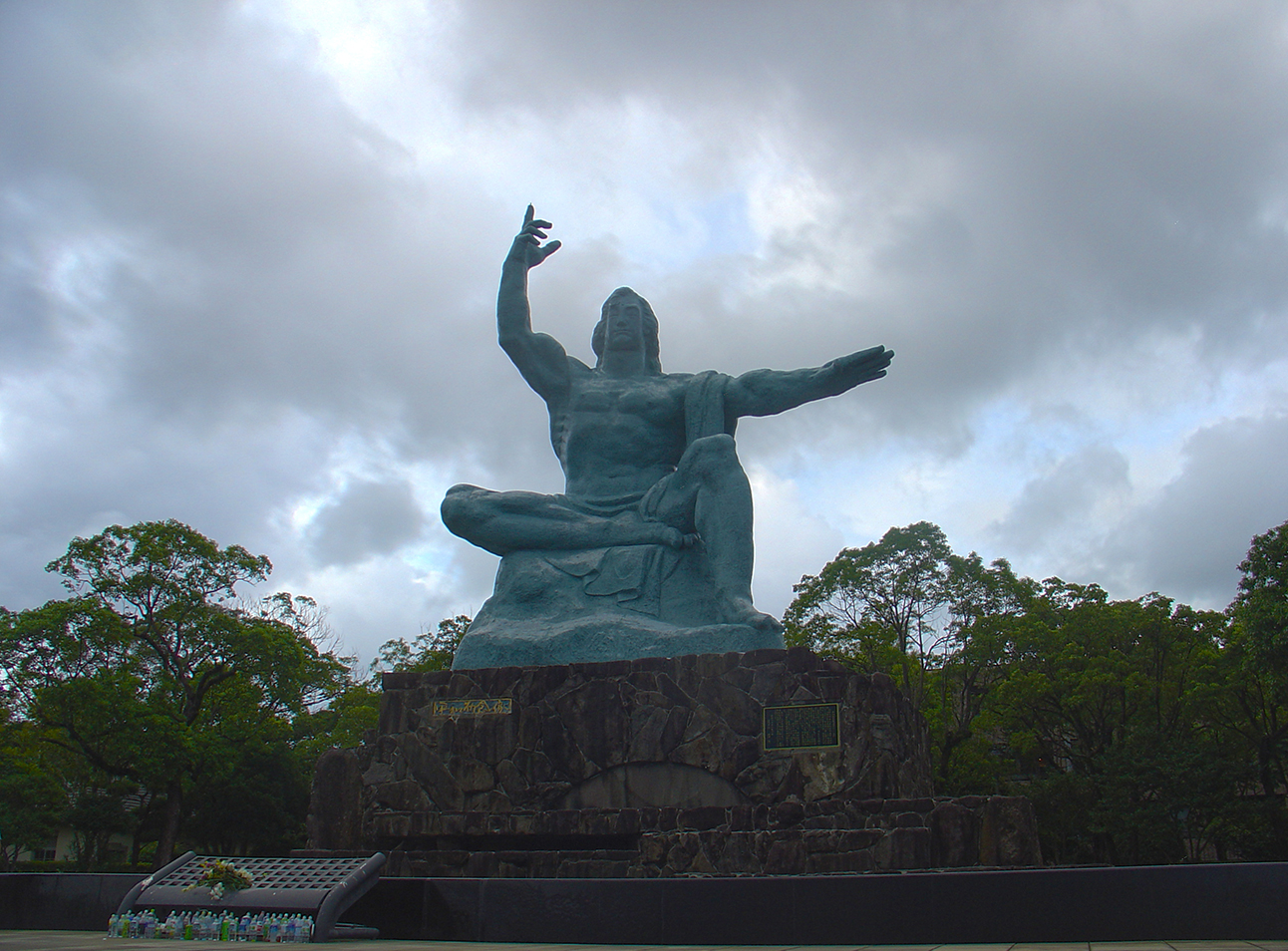 The right hand points to the sky, where the atomic bomb exploded; the left hand points towards peace.